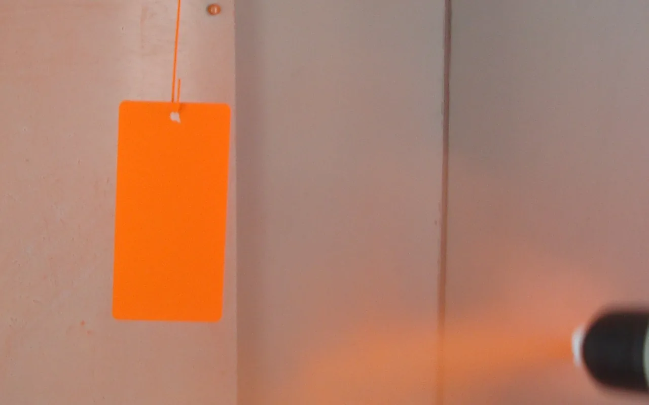 Powder coating being applied to a suspended metal panel.
